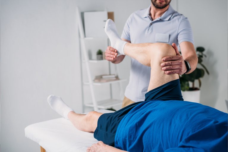 Physiotherapeut führt krankengymnastische Übungen am Bein eines Patienten durch