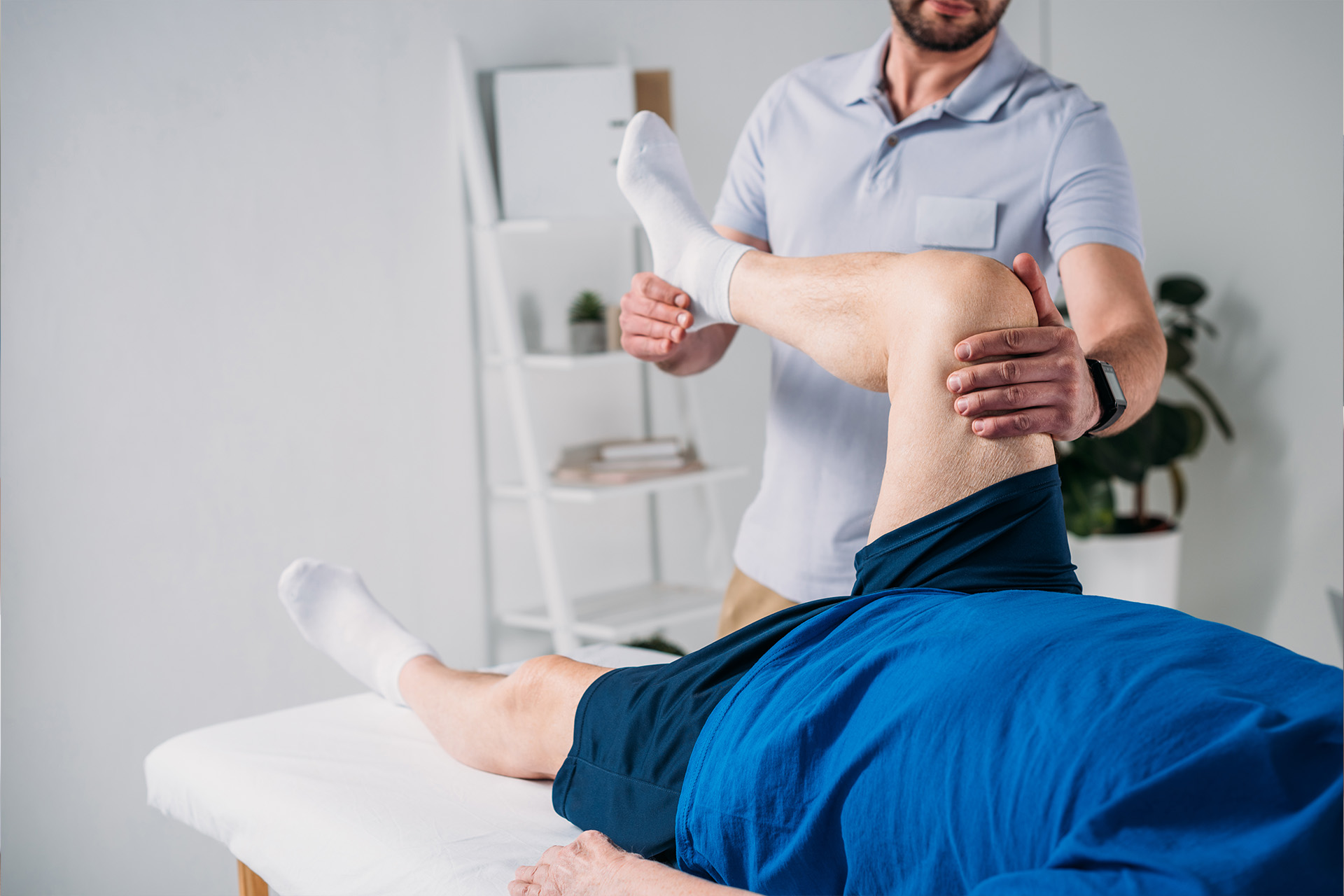 Physiotherapeut führt krankengymnastische Übungen am Bein eines Patienten durch