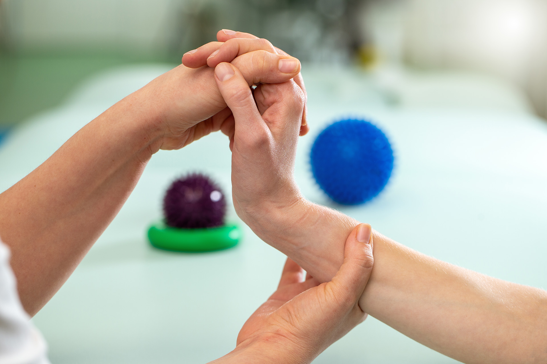 Nahaufnahme der zwei Hände eines Physiotherapeuten, der mit mit Hilfe manueller Therapie ein Handgelenk behandelt