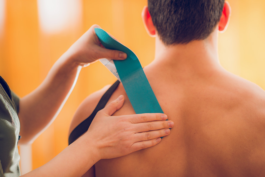Nahaufnahme des Anbringens eines Kinesiotapes auf dem Rücken eines Patienten in einer Praxis für Physiotherapie