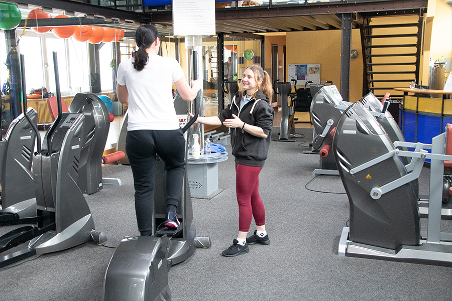 Physiotherapeutin im Physio-Point Hamburg leitet Patientin beim Training auf einem Crosstrainer im Medizinischen Fitnesscenter an