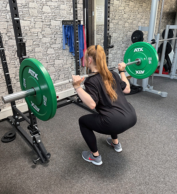 Junge Frau trainiert in medizinischem Fitnessstudio mit einer Langhantel